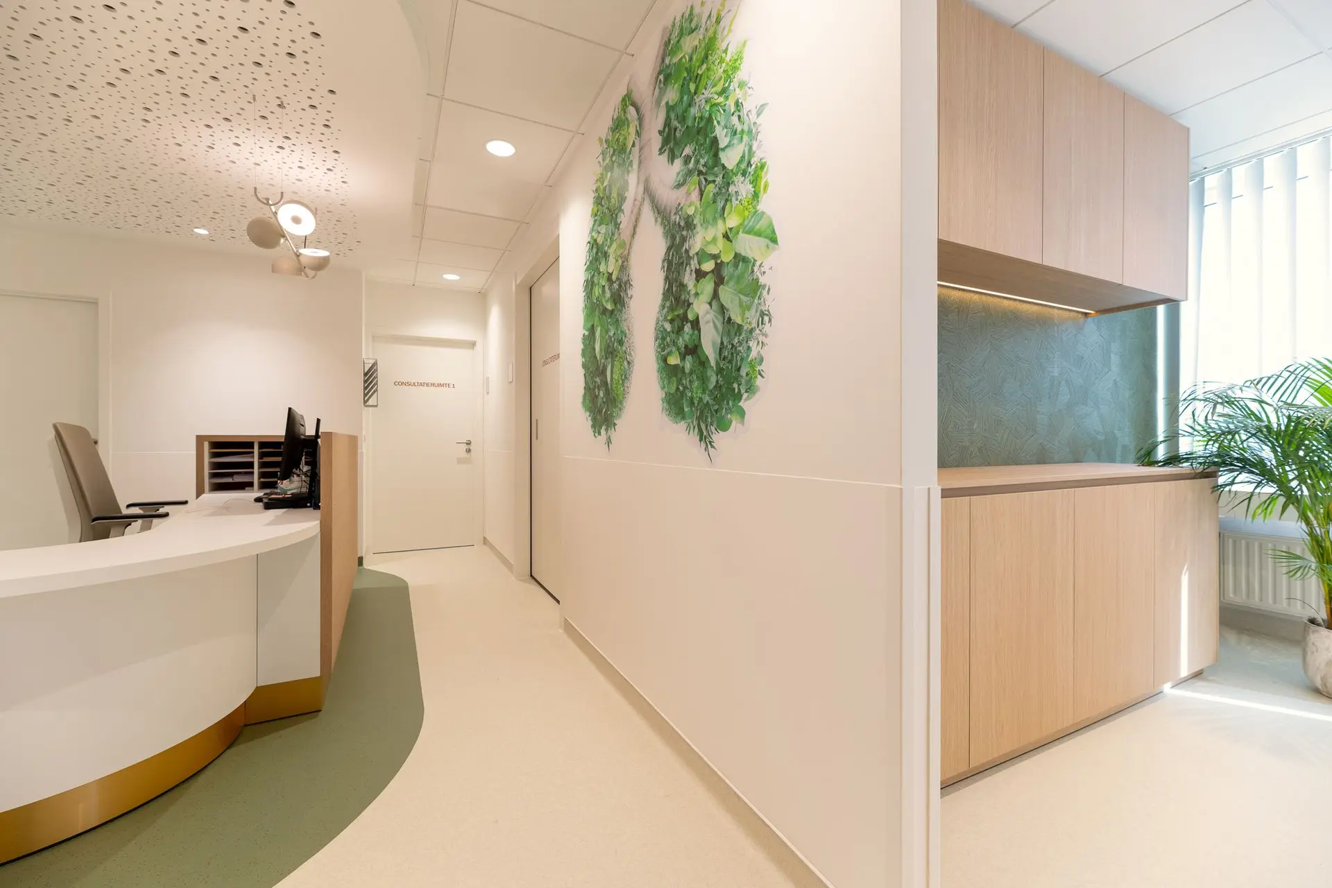 Modern onthaal met maatwerkinterieur en groene wanddecoratie in de vernieuwde longartsenpraktijk van Sint-Truiden.