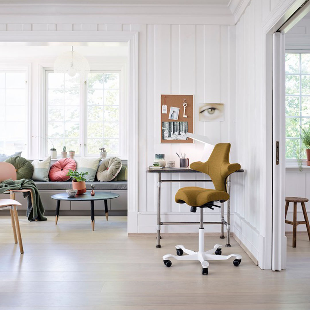 HÅG Capisco 8106 in mosterdgeel aan een hoog bureau in lichte woonkantooromgeving