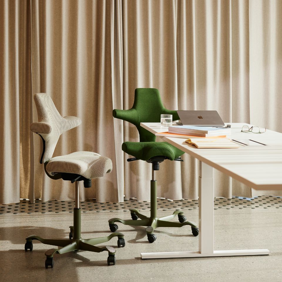 Twee HÅG Capisco 8106 stoelen in groen naast een wit zit-sta bureau in lichte kantooromgeving