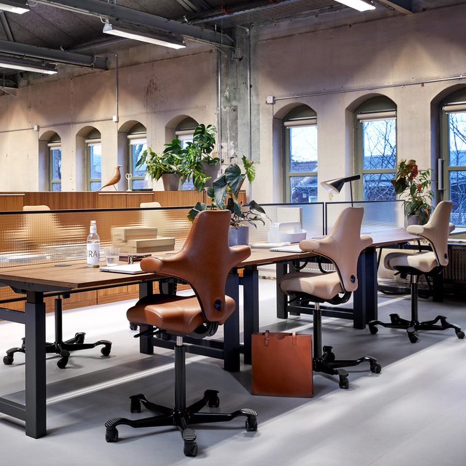Rij HÅG Capisco 8106 stoelen in cognacbruin leder in open industrieel kantoor met bogen