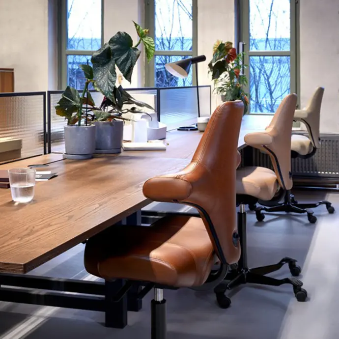 HÅG Capisco 8106 in cognacbruin leder aan houten vergadertafel in industrieel kantoor