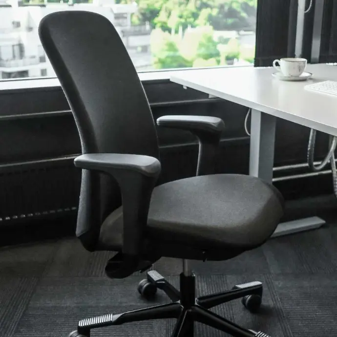 Zwarte HÅG SoFi 7300 met volledig gestoffeerde rugleuning en armleuningen voor langdurig zitcomfort Zwarte HÅG SoFi 7300 bureaustoel met armleuningen naast bureau