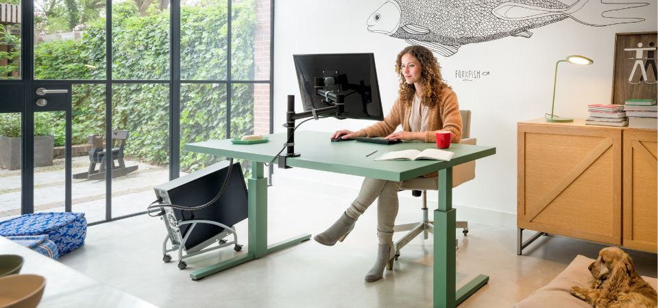 Ergonomische thuiswerkplek met een zit-sta bureau en slimme kabelbeheeroplossing voor meer comfort en productiviteit. Moderne thuiswerkplek met een groene zit-sta bureau, ergonomische monitorarm en een kabelmanagementsysteem voor een opgeruimd bureau.