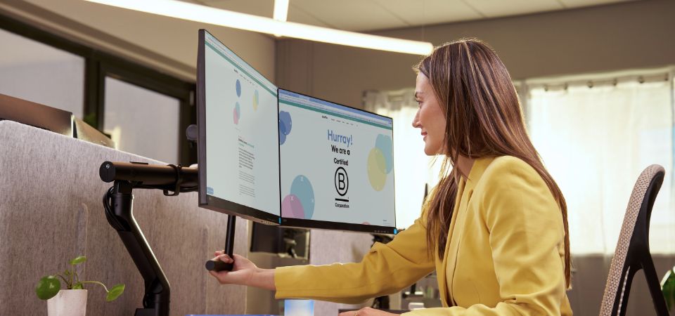 Ergonomische monitorarm voor een optimale schermhoogte en een comfortabele werkhouding. Vrouw stelt haar monitor in op de juiste hoogte met een ergonomische monitorarm voor een betere werkhouding en minder nekbelasting.
